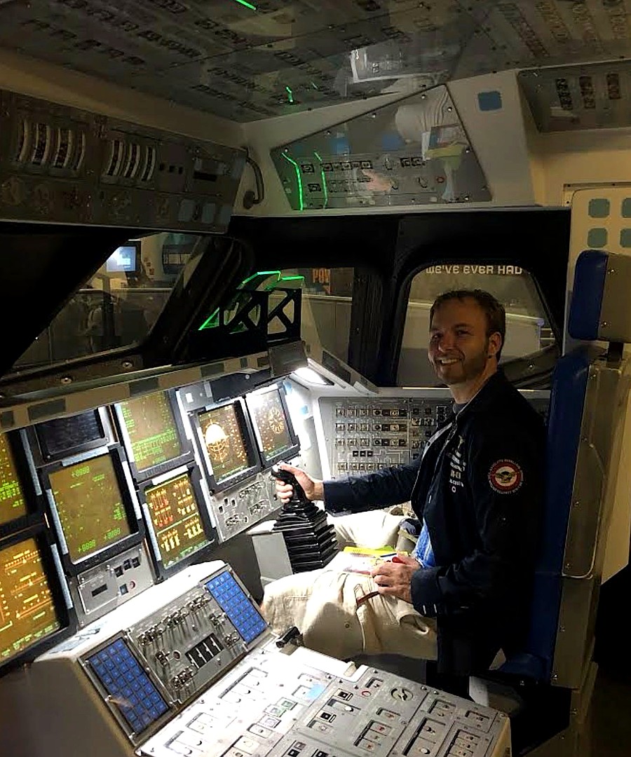At a space shuttle flight-deck exhibit, flight jacket visible